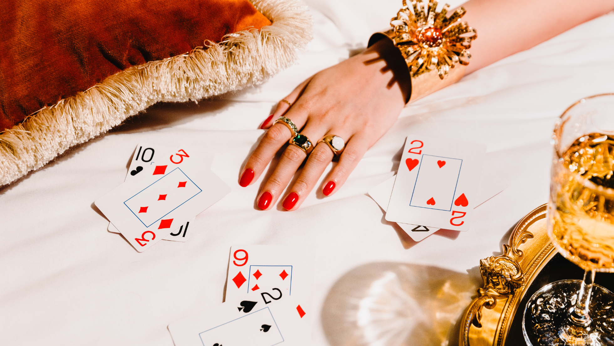 hand with red nail polish surrounded by playing cards and a cocktail